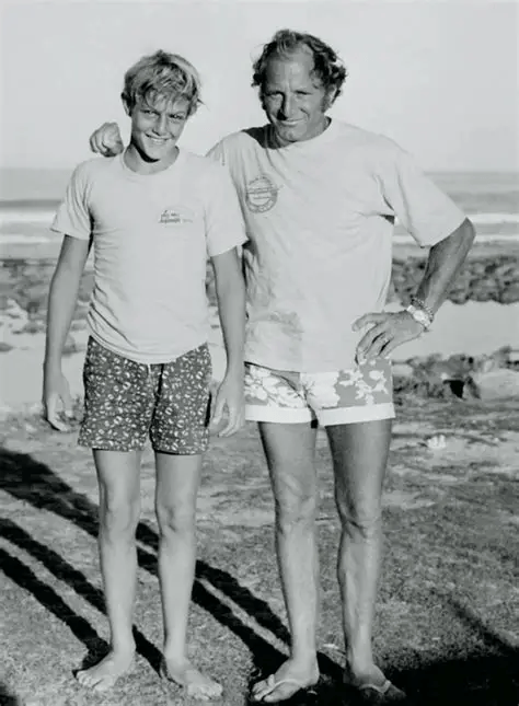 Young Shaun Tomson standing with his father Ernest Tomsoon on a South African beach, reflecting the family values and resilience that shaped his surfing and leadership journey.