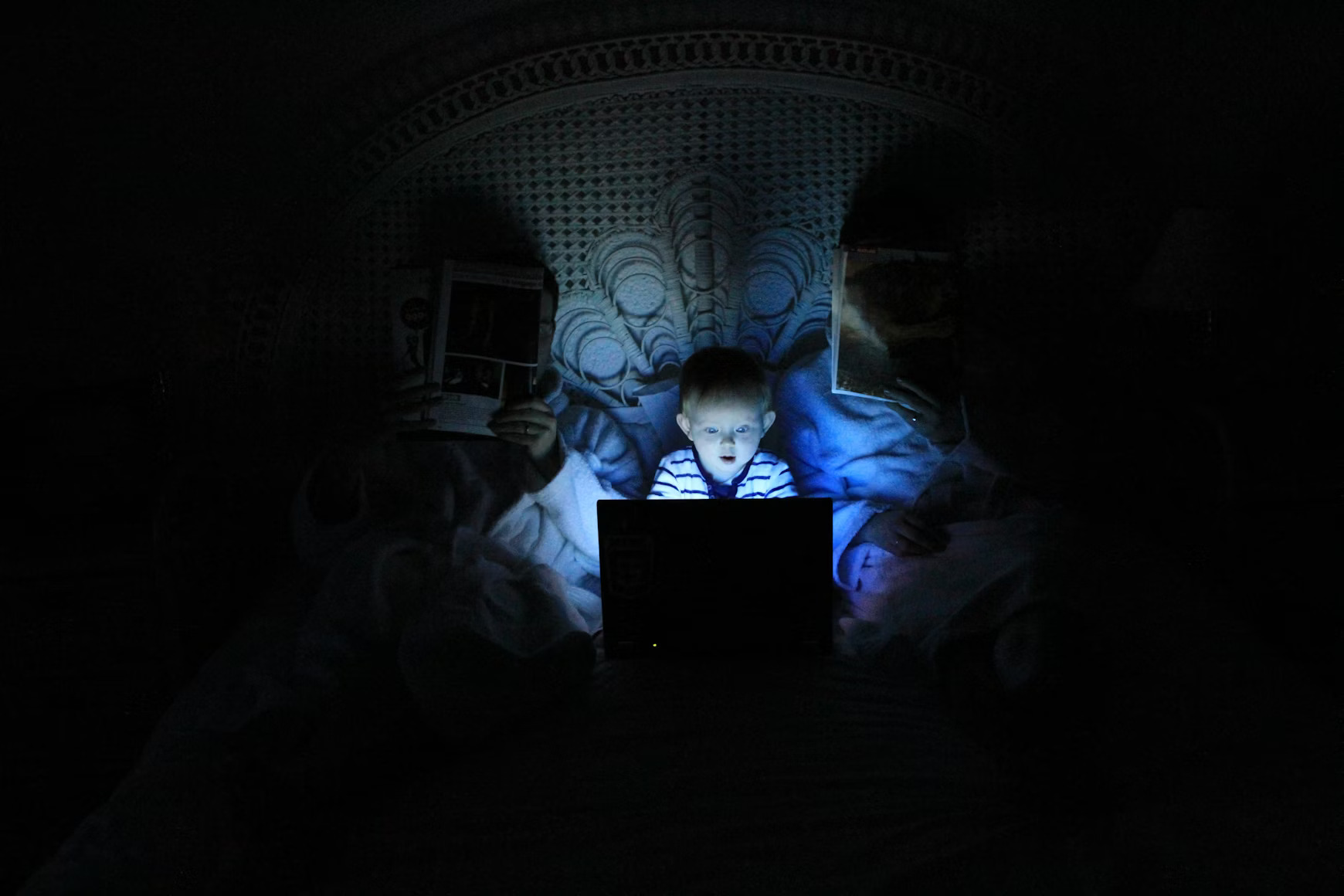 Young child using a laptop at night, highlighting the need for online safety measures.