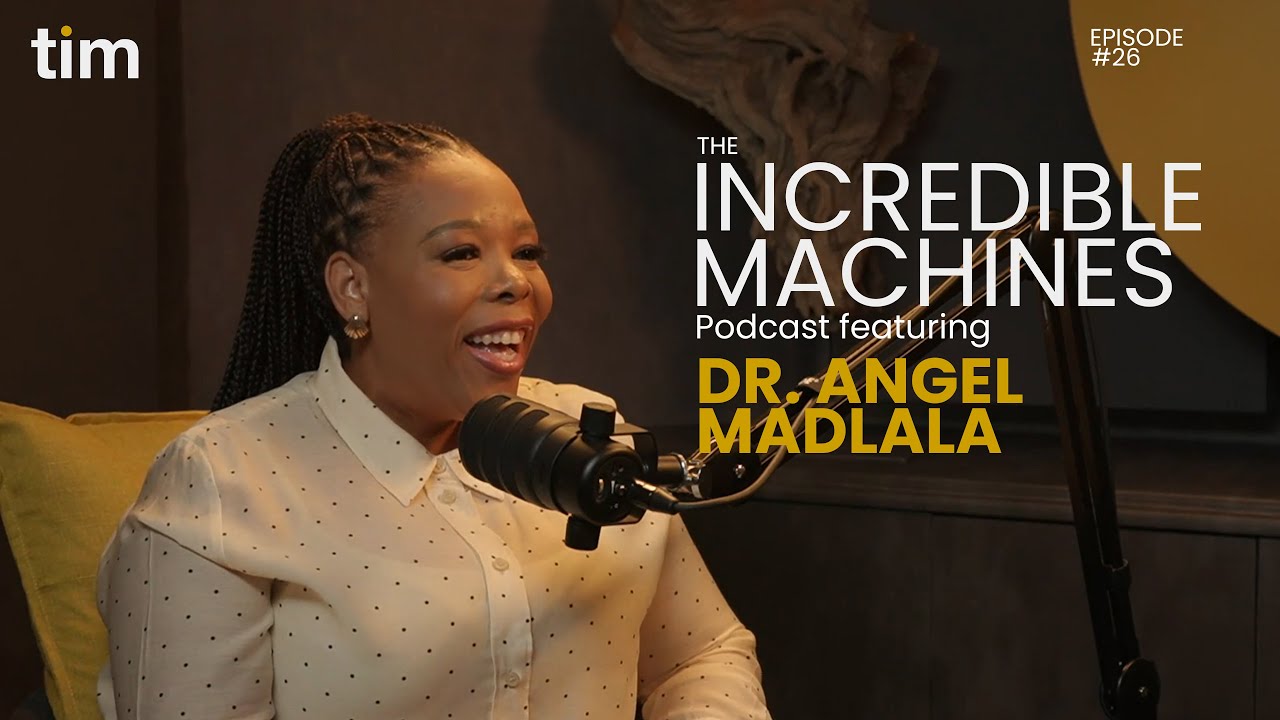 Dr Angel Madlala smiling while speaking into a podcast microphone during Episode 26 of The Incredible Machines Podcast by Tim Africa. The mustard yellow and black Tim Africa studio background is visible.