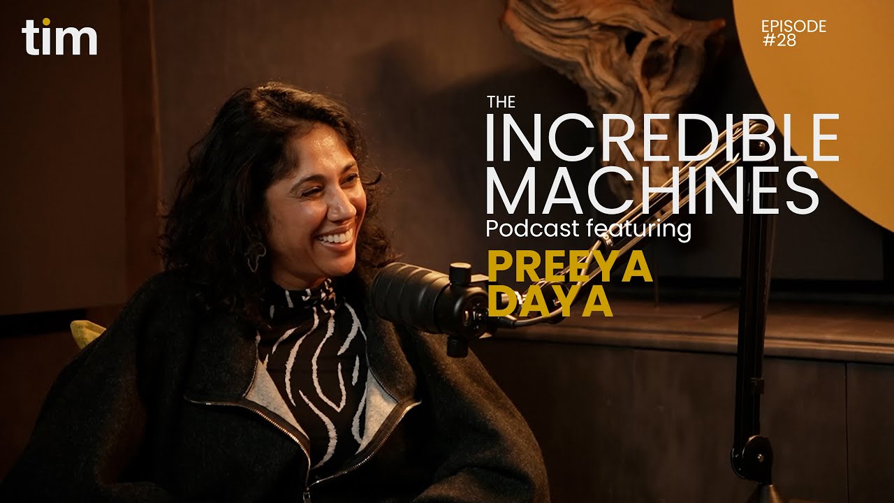 Dr Preeya Daya in conversation on The Incredible Machines Podcast Episode 28, seated in Tim Africa’s mustard and black studio, smiling as she speaks into a broadcast mic.