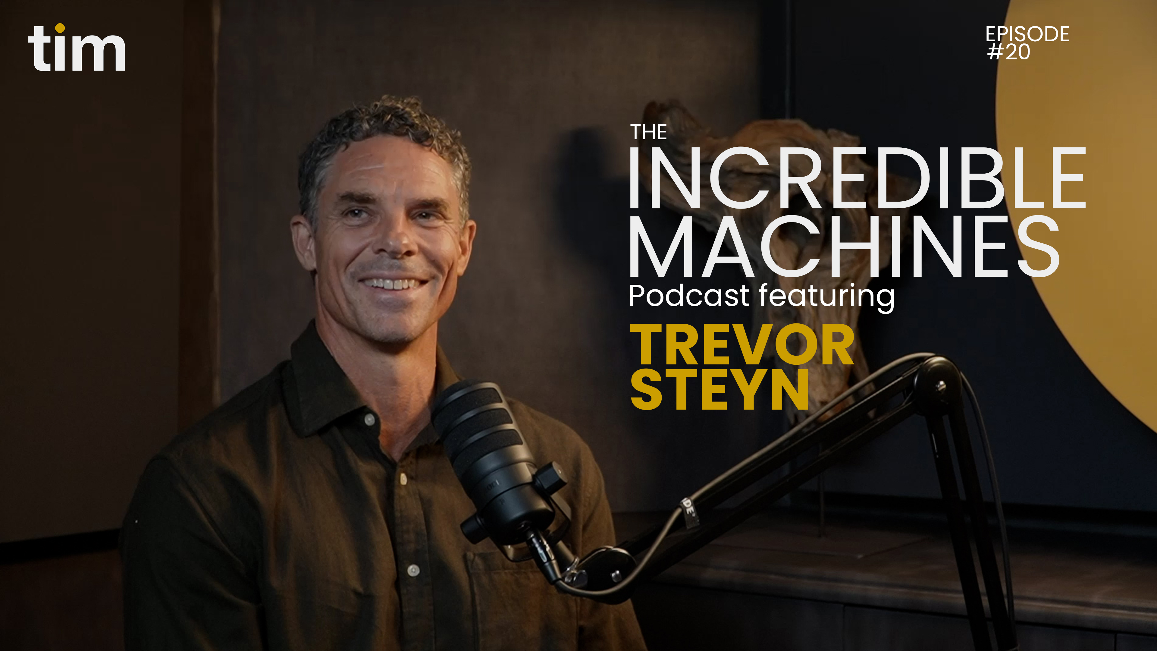 Trevor Steyn, featured guest on Episode 20 of The Incredible Machines Podcast by Tim Africa, smiling confidently while seated behind a podcast microphone in the signature mustard and black podcast studio.