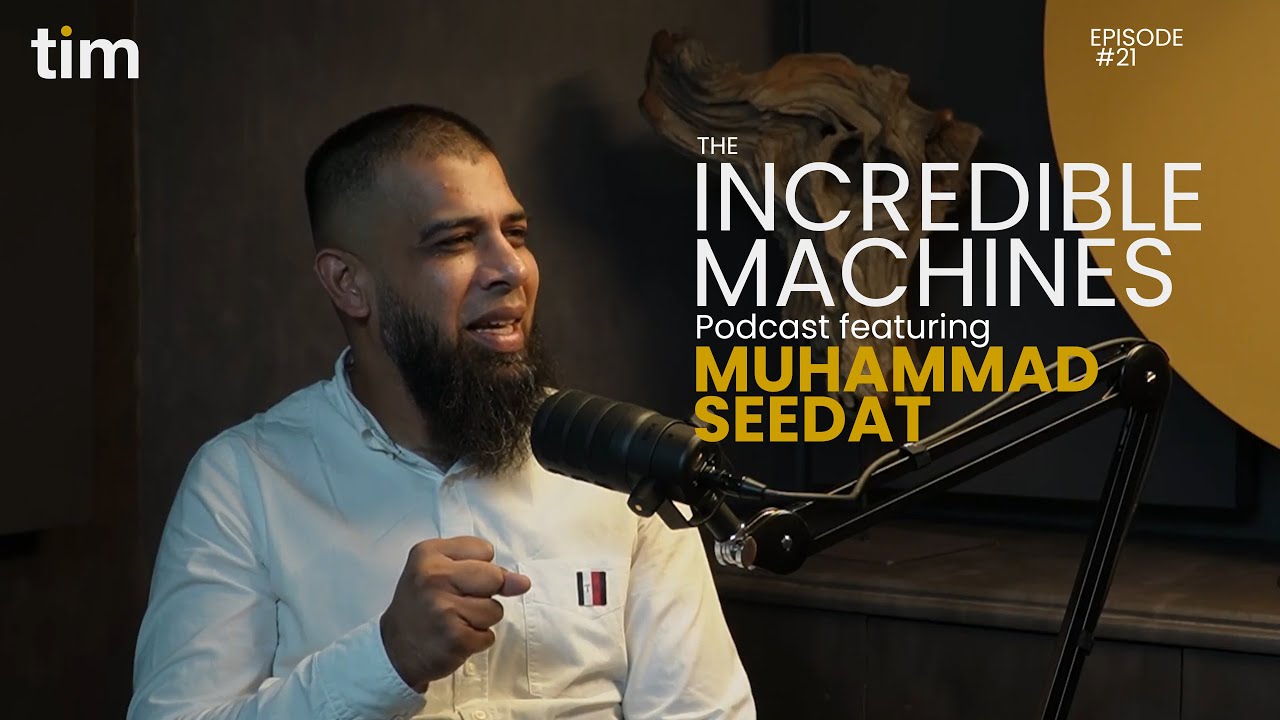 Muhammad Seedat gesturing while speaking on The Incredible Machines Podcast Episode 21, filmed in Tim Africa’s mustard and charcoal-toned podcast studio.