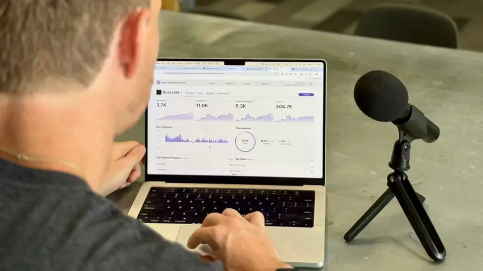 A podcaster reviewing listener analytics on a laptop beside a microphone